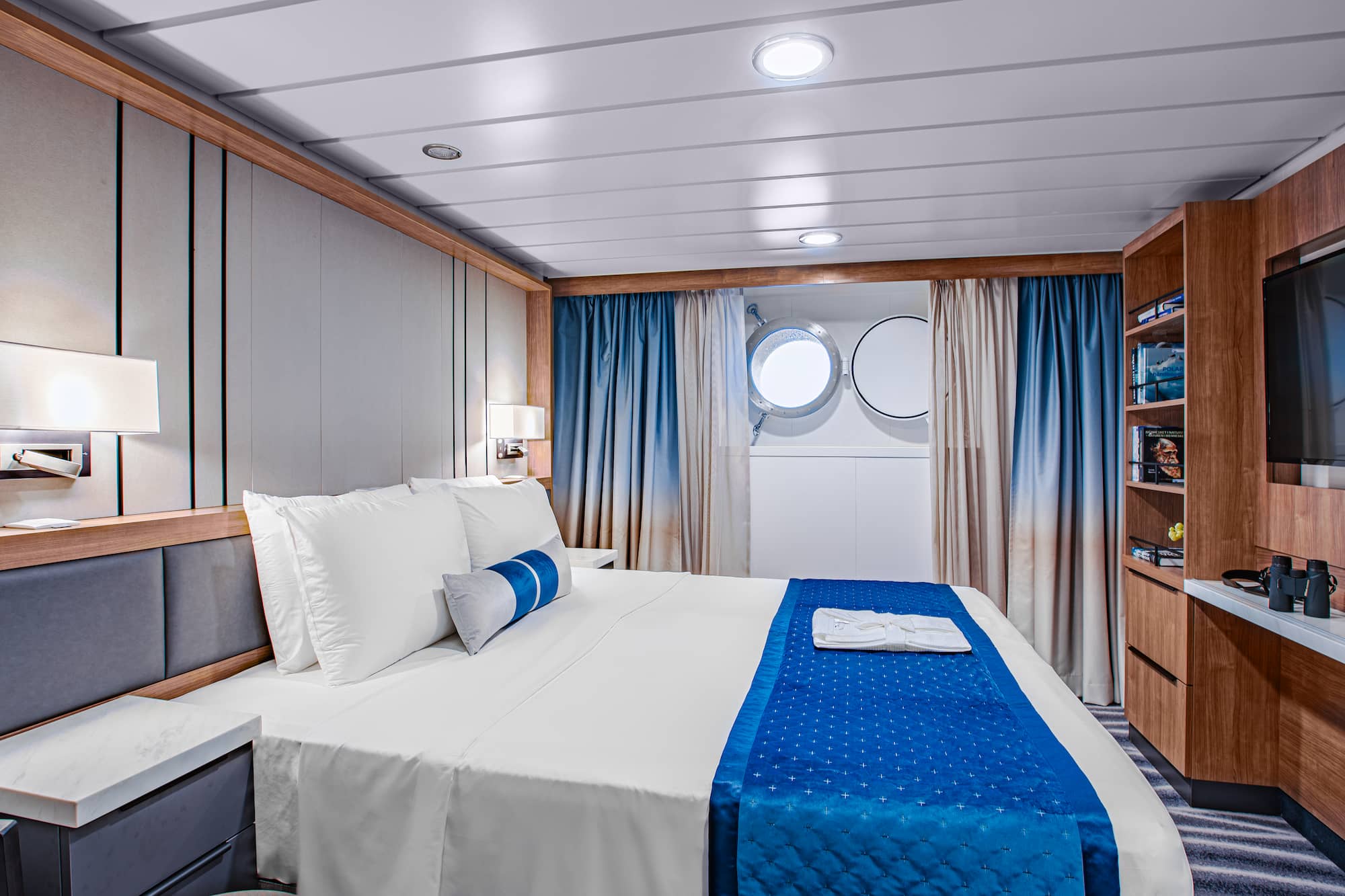 Interior of a porthole cabin on an Antarctica expedition cruise ship, showing a double bed and a round sea-level window.