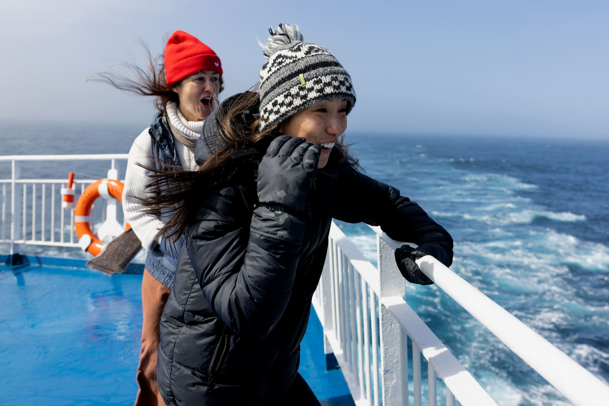 Two passengers laughing in the wind on the deck of an expedition cruise ship crossing the Drake Passage to Antarctica.