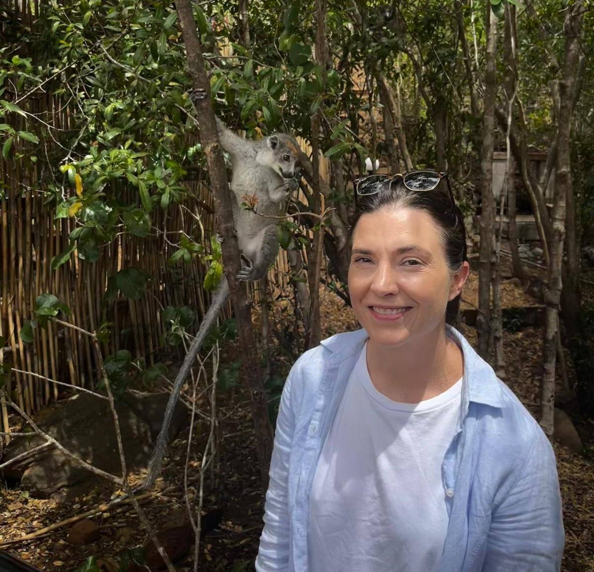 Smiling traveller with a curious grey lemur perched on a branch beside her, Nosy Komba Island, Madagascar.