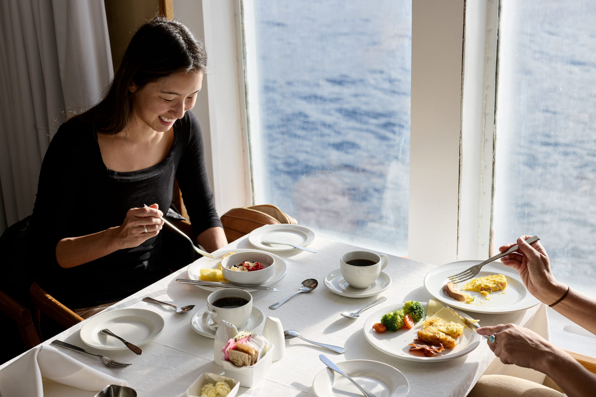 Passenger dining on an expedition cruise ship with the Southern Ocean visible through the window during the Drake Passage crossing.
