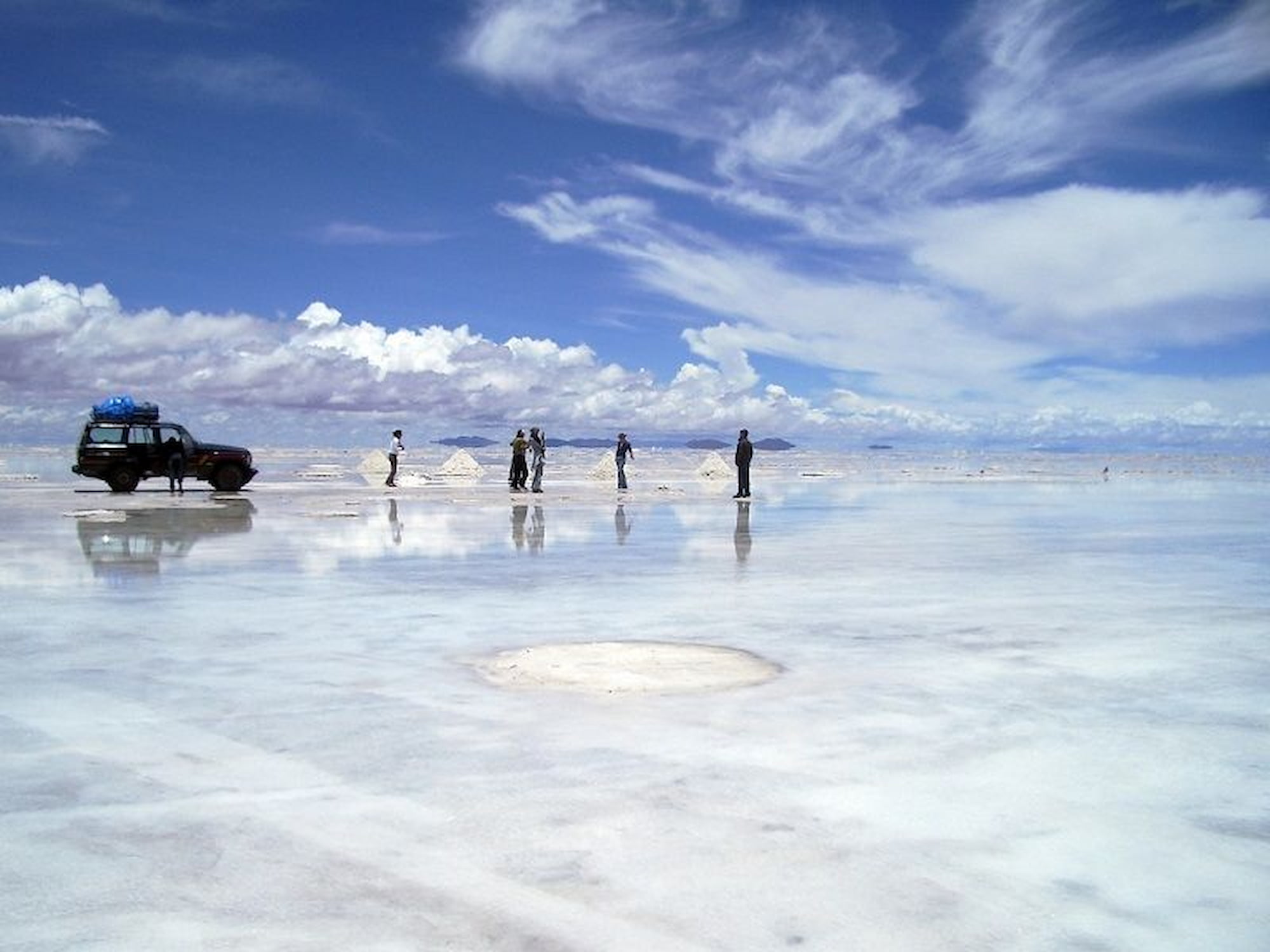 Sky reflected on the flooded Uyuni Salt Flats during rainy season, with tourists and 4WD vehicle, Bolivia