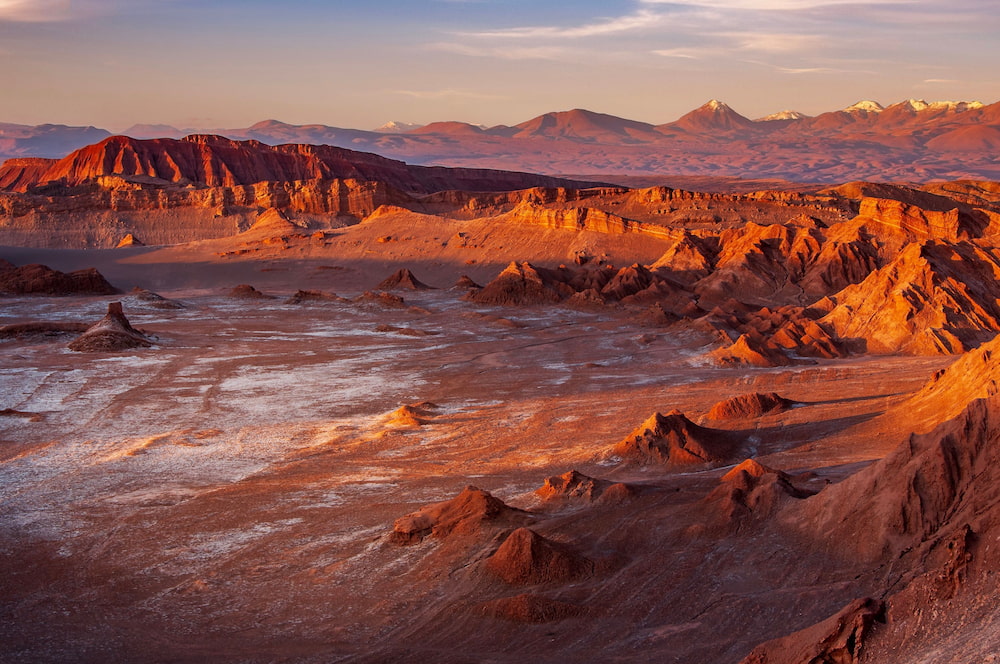 Sunset over the Valle de la Luna in Chile’s Atacama Desert, with rugged red rock formations, salt flats, and distant snow-capped peaks.
