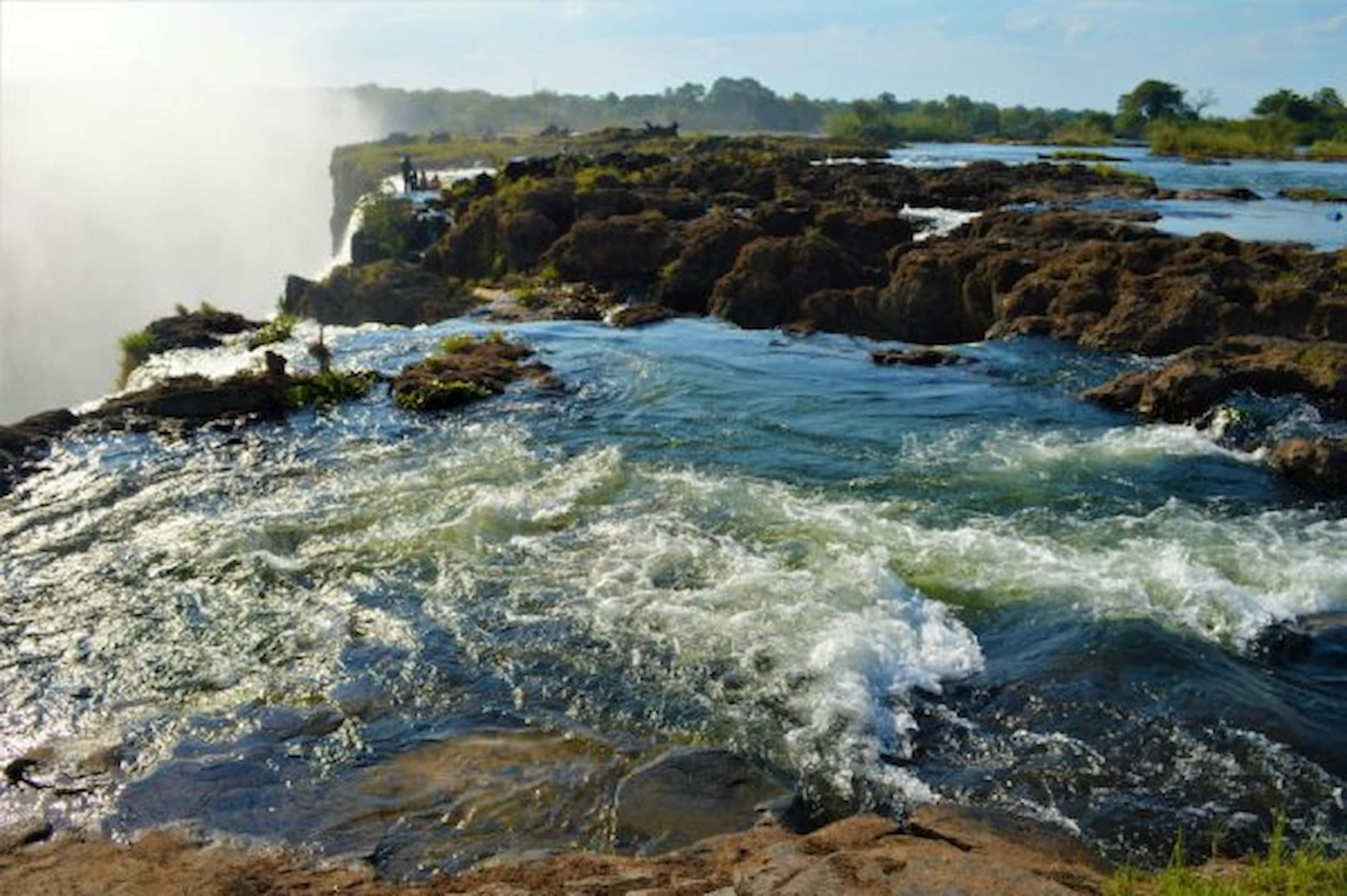 Turbulent waters and mist rising from Victoria Falls as they cascade over the rocky edge into the Zambezi River
