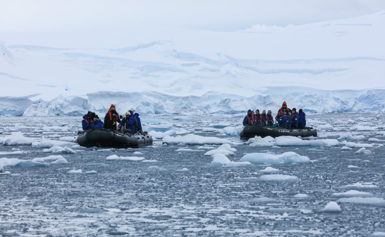 Crossing the Antarctic circle guest on zodiac navigating through icy waters with massive glaciers in the background