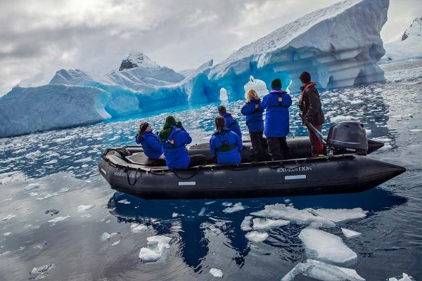 Group of people in a zodiac boat with large iceberg in background