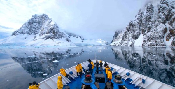 People in yellow jackets on the bow of a ship in Antarctica