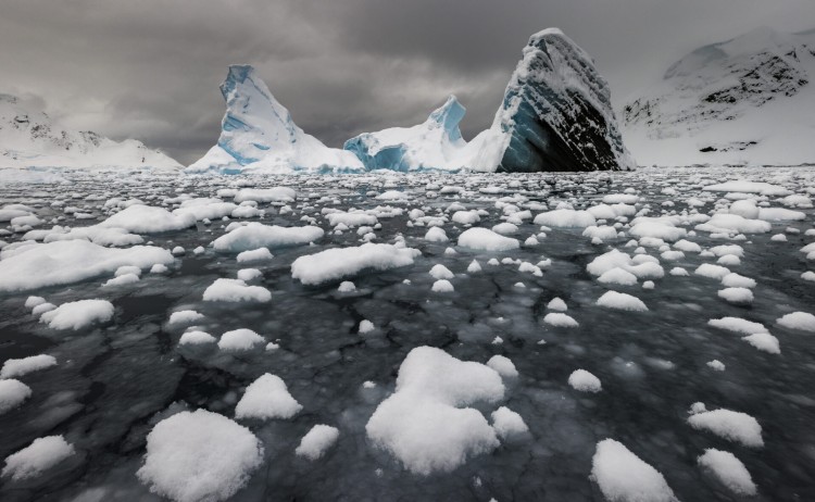 Iceberg rising above a sea of nylas ice and small ice floes covered in fresh snow Paradise Harbour Antarctica Richard IAnson scaled