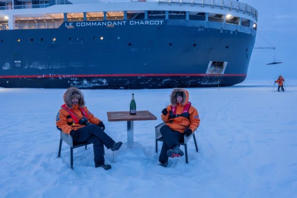 Two people sitting on chairs on the ice, in front of Le Commandant Charcot