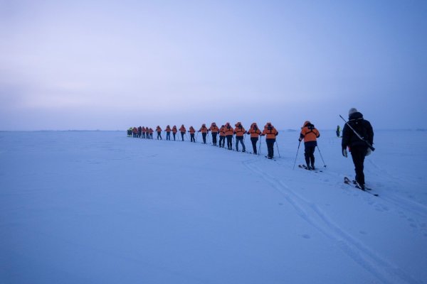 Line of people cross country skiing across a flat white landscape