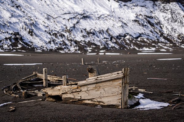 Wreck of an old fishing boat lies semi-buried on Deception Island in Antarctica