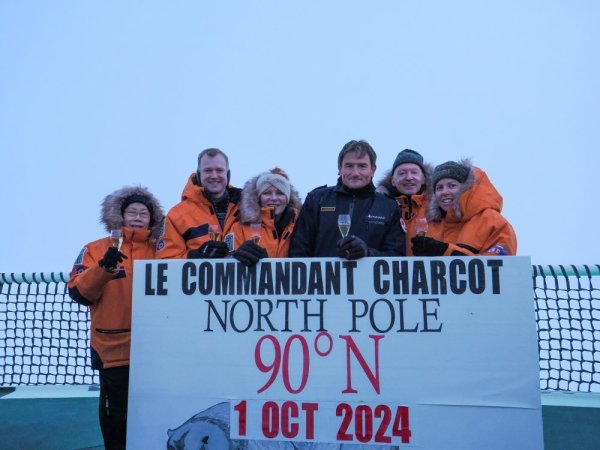 Group of people in orange coats, holding a sign at the North Pole