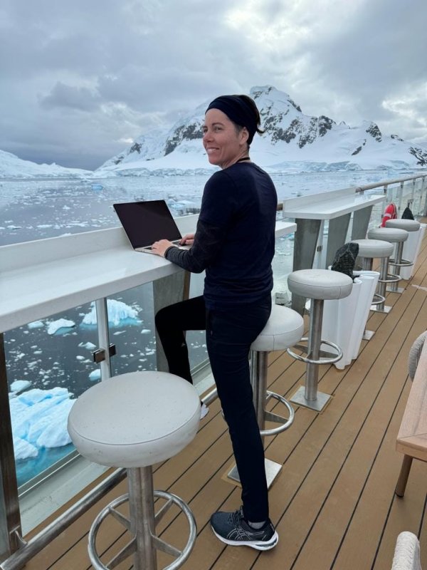 Person working on a laptop on the ship's deck, with icebergs in the background