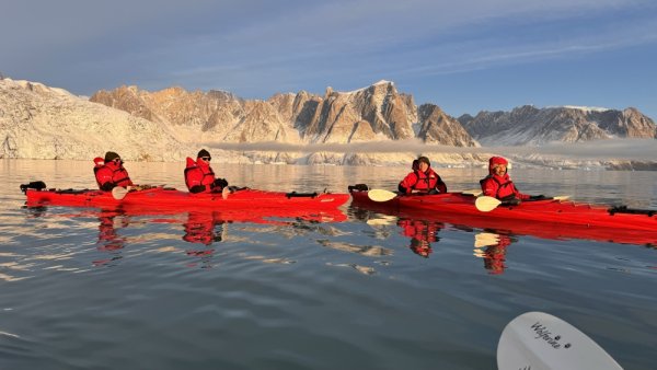 Two red double kayaks in calm water with rocky cliffs in the background