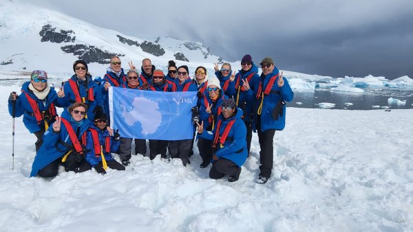 Group of guests in Antarctica wearing blue jackets, holding a blue flag