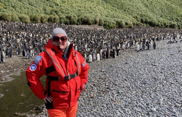 Woman in red standing in front of large penguin colony on rocky shore