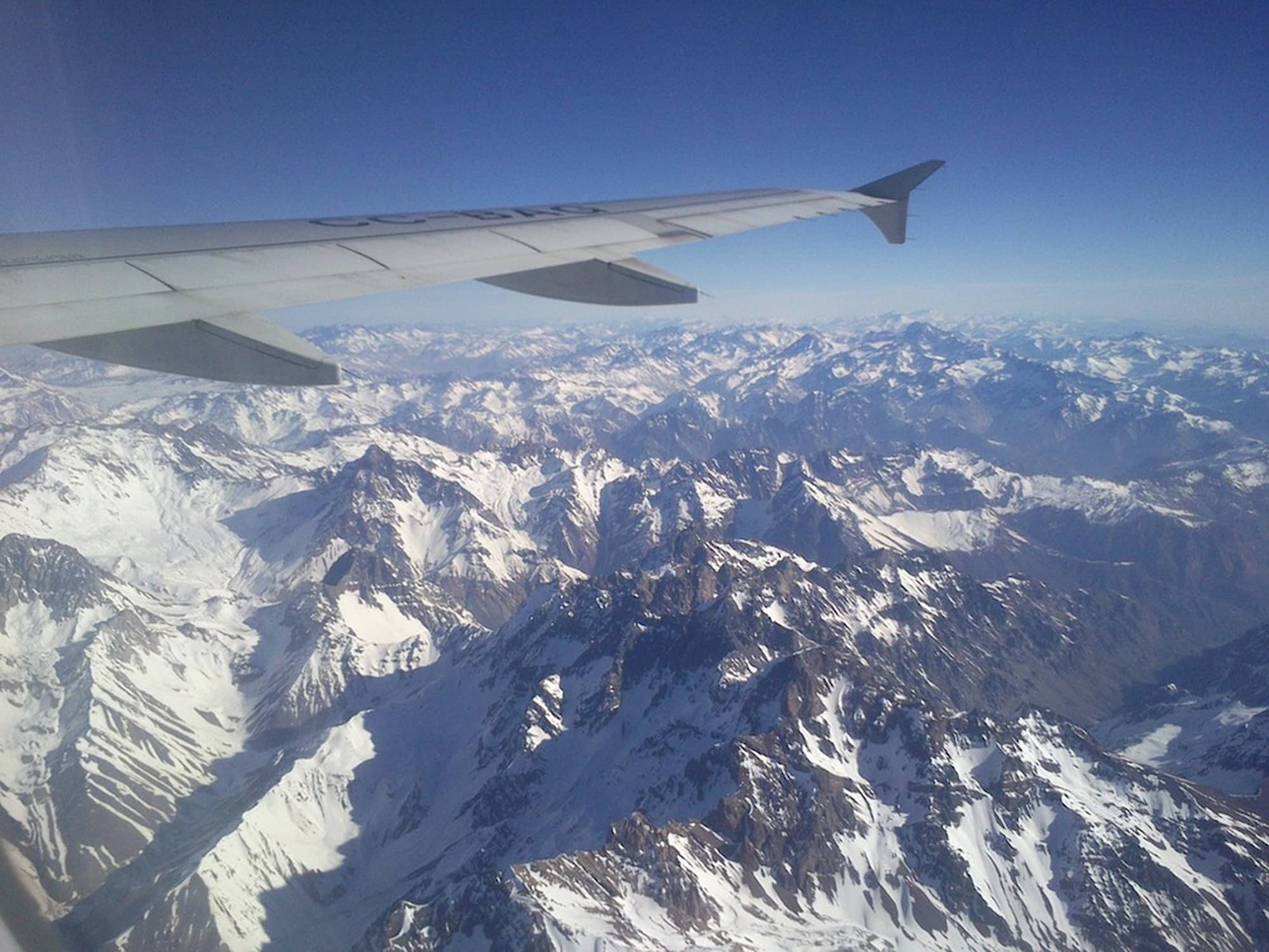 View of the snow-capped Andes mountains from a plane window — direct flights from New Zealand to South America.