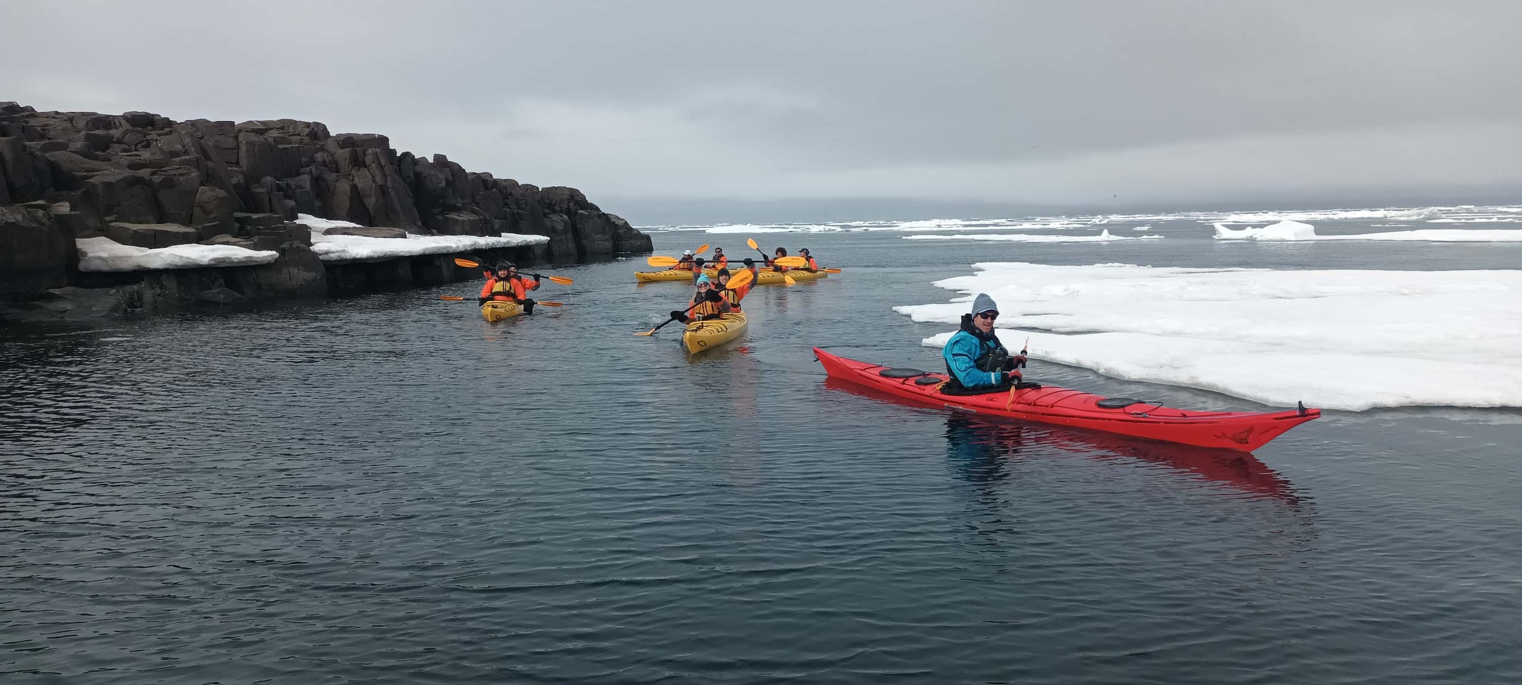 Kayakers paddling near shore among sea ice during Ultramarine Arctic voyage.