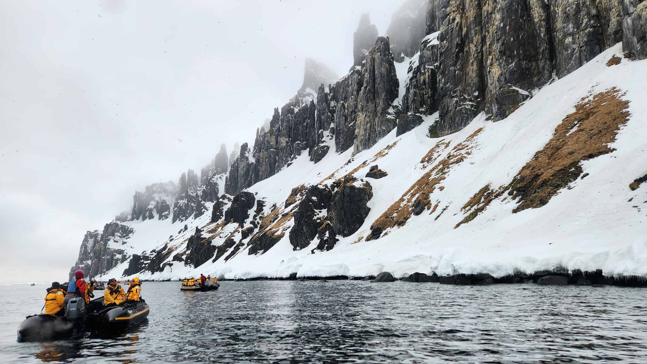 Zodiac boat with passengers exploring snowy cliffs and fjords in Svalbard during an Arctic cruise expedition.