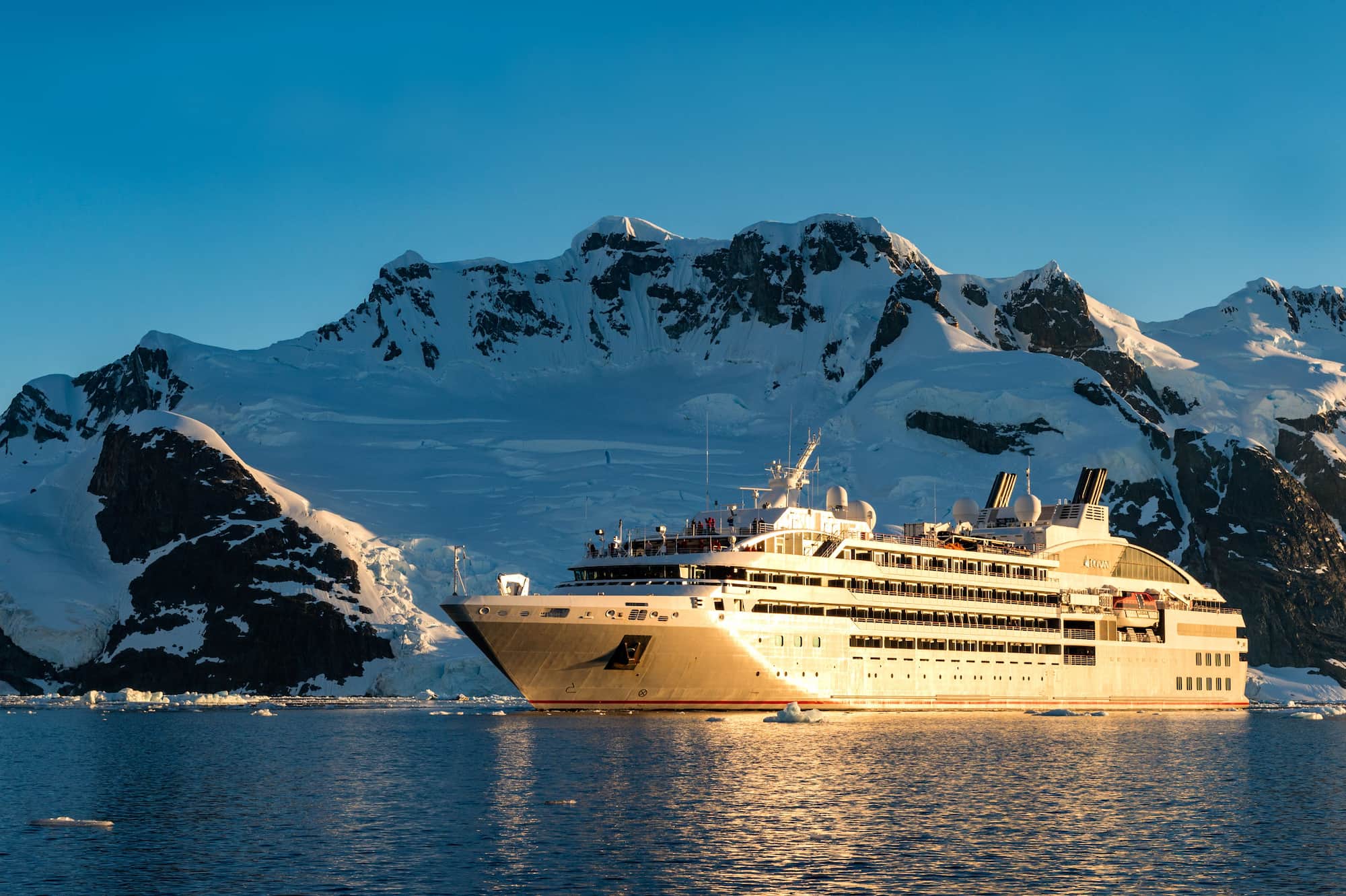 Ponant expedition cruise ship anchored in Antarctica with snow-capped mountains in the background.