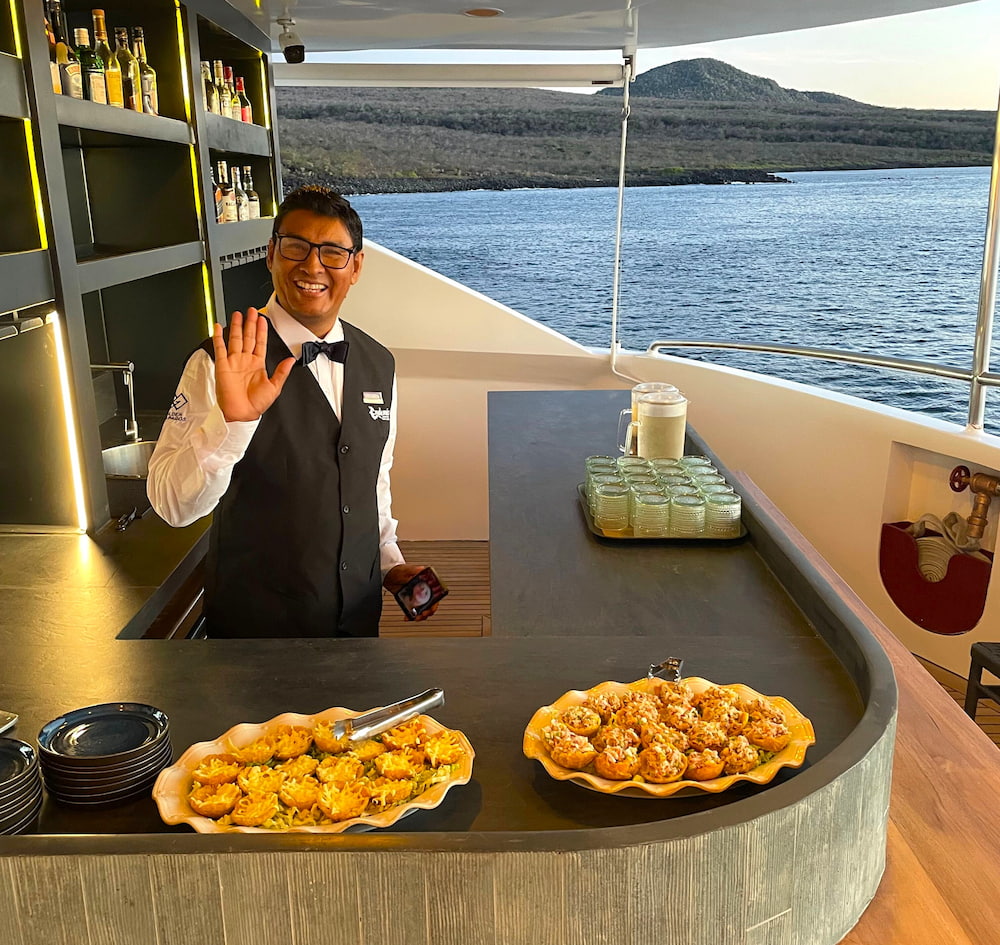 Barman serving canapes and drinks on the sun deck of M/C Endemic Galapagos cruise catamaran at sunset