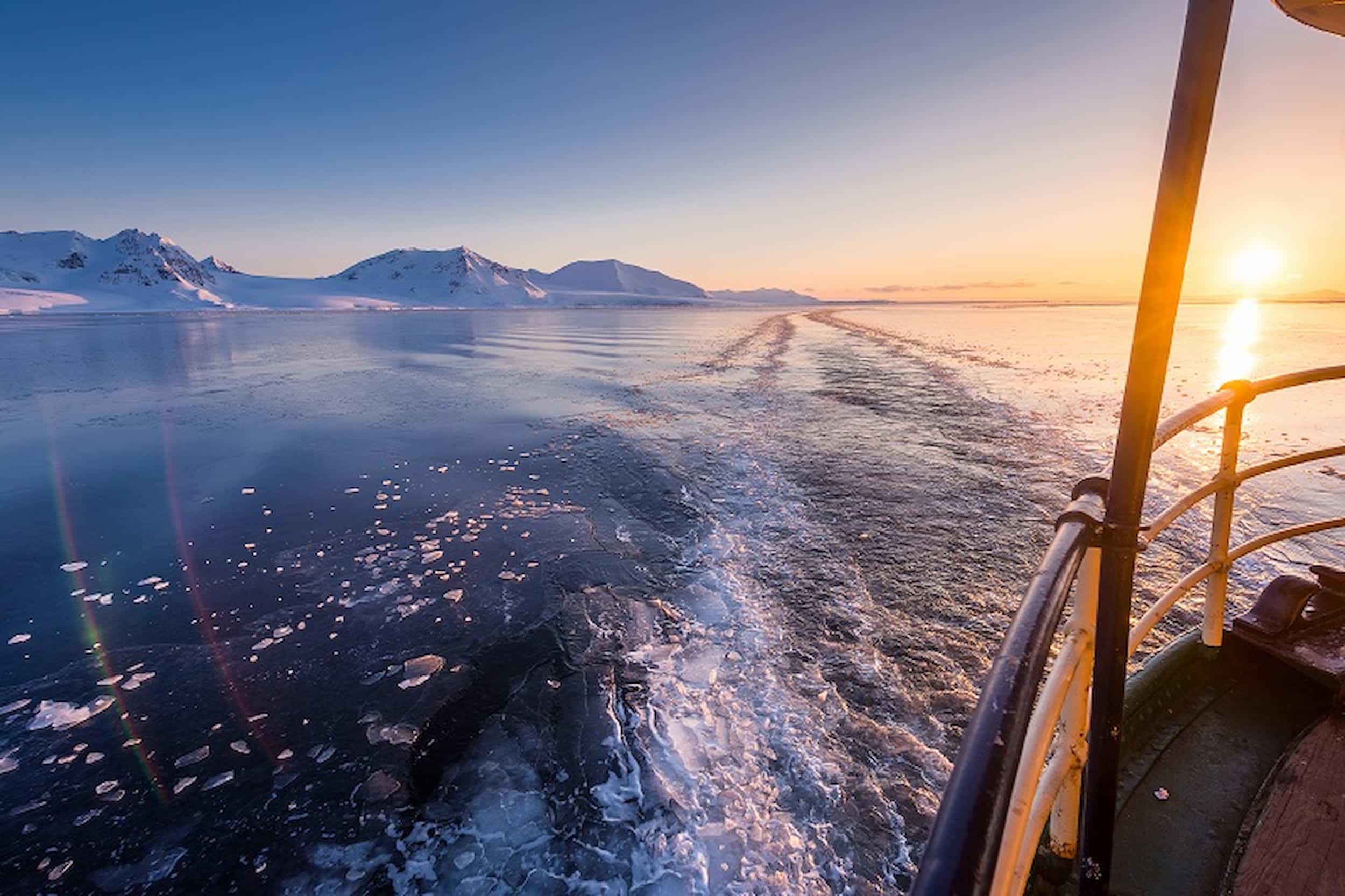 Polar expedition cruise at sea, with the sun setting and mountains in the background.