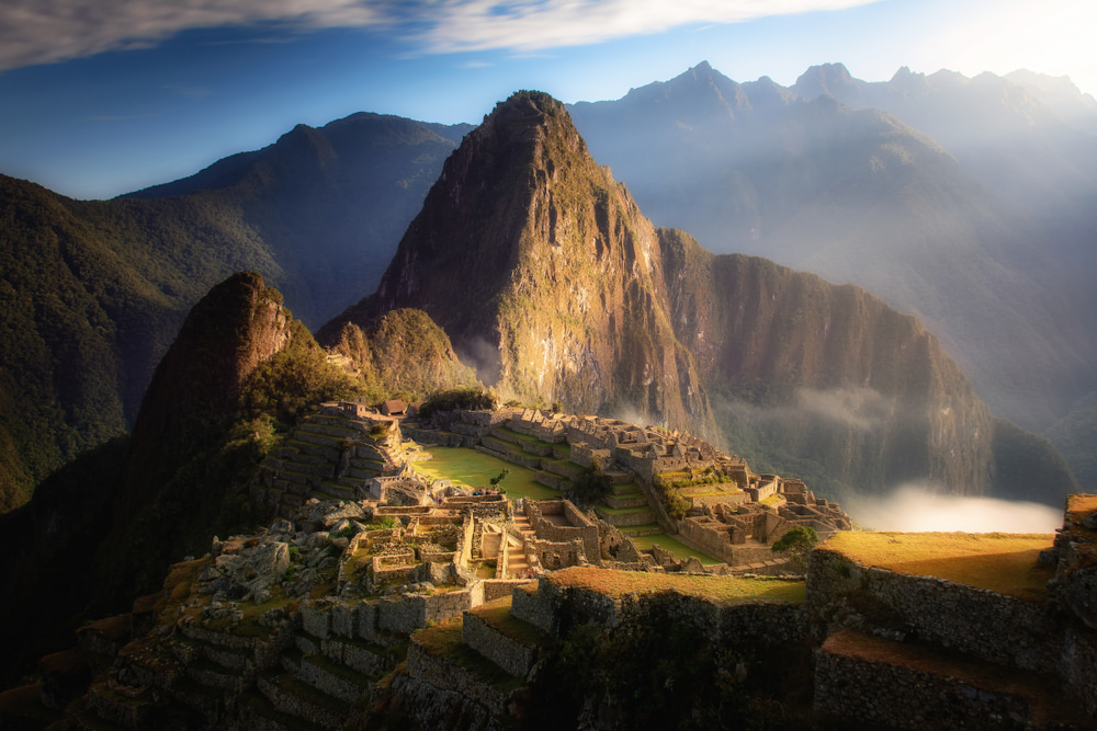 View of Machu Picchu at sunrise from the Sun Gate, with golden light illuminating the citadel and surrounding Andes. View of Machu Picchu at sunrise from the Sun Gate, with golden light illuminating the citadel and surrounding Andes.