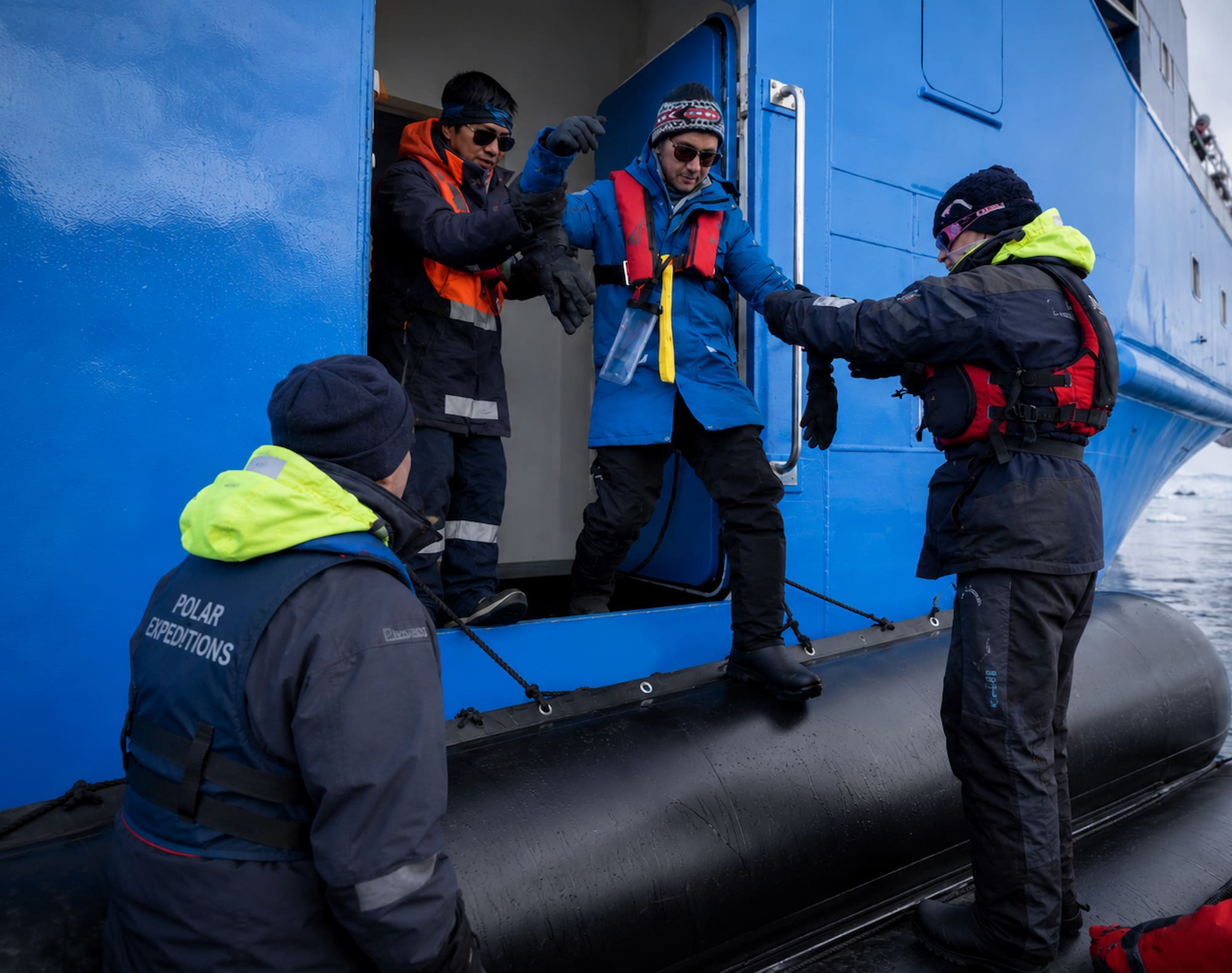 Expedition crew helping a guest step into a Zodiac boat during a polar cruise