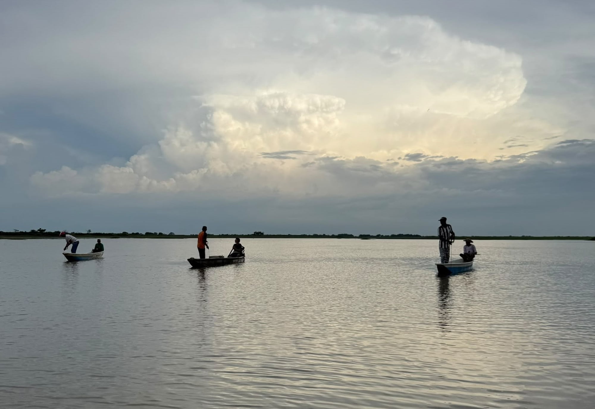 Fishermen in small wooden canoes on the calm Magdalena River under a cloudy evening sky, Colombia.