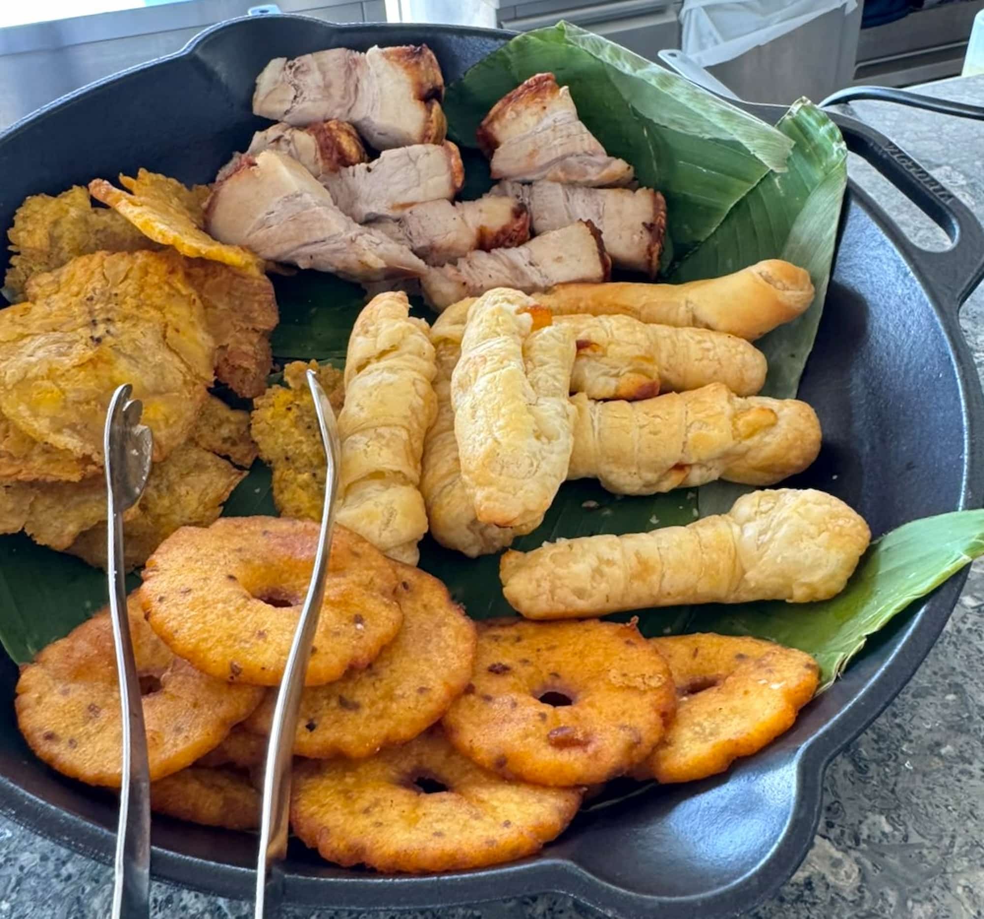 Cast-iron pan of fried Colombian snacks on a banana leaf, including patacones and cheese-filled pastry sticks, served aboard the AmaMelodia on the Magdalena River, Colombia.