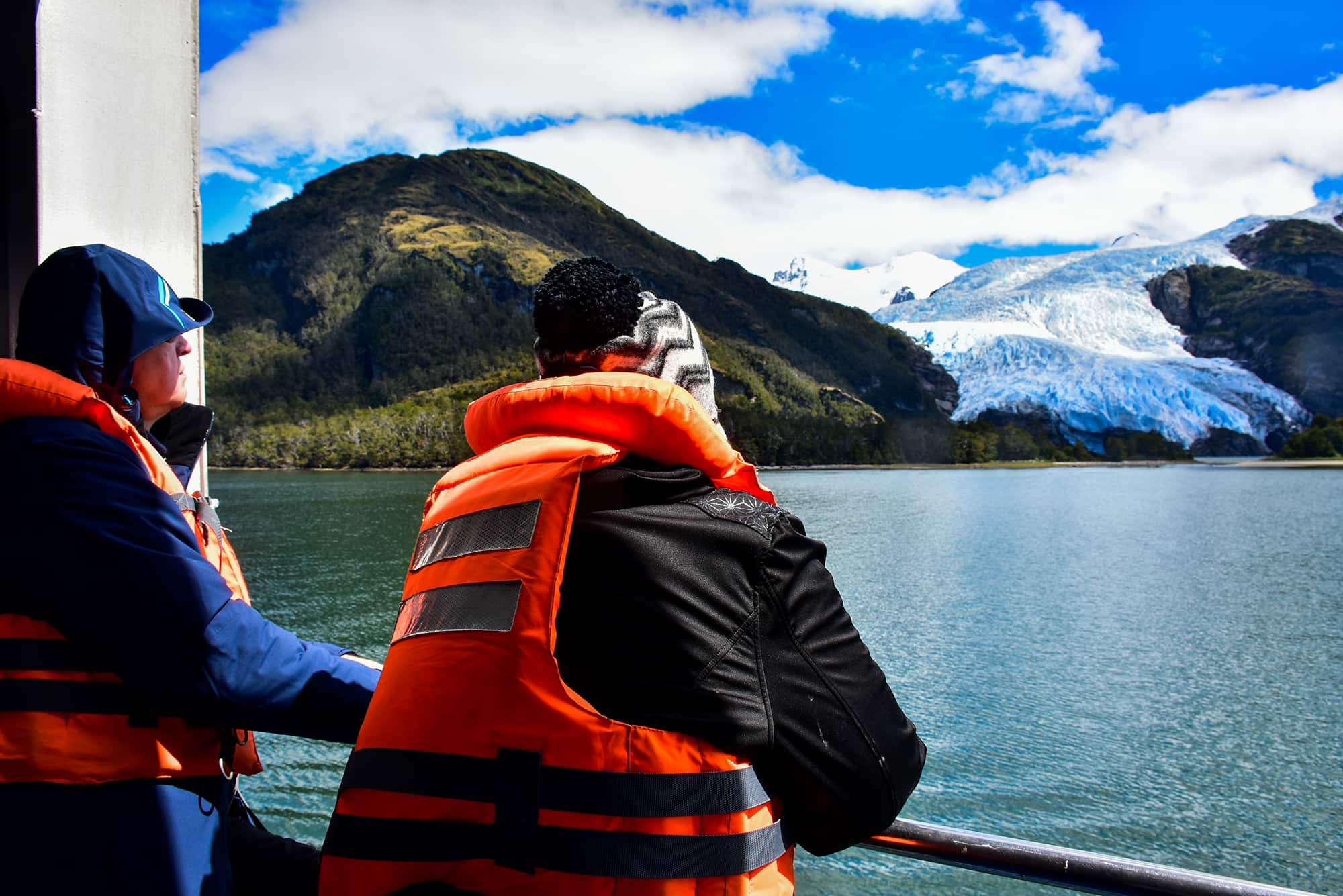 Travellers in life jackets on the deck of a boat looking out at a tidewater glacier, Tierra del Fuego, Chilean Patagonia.
