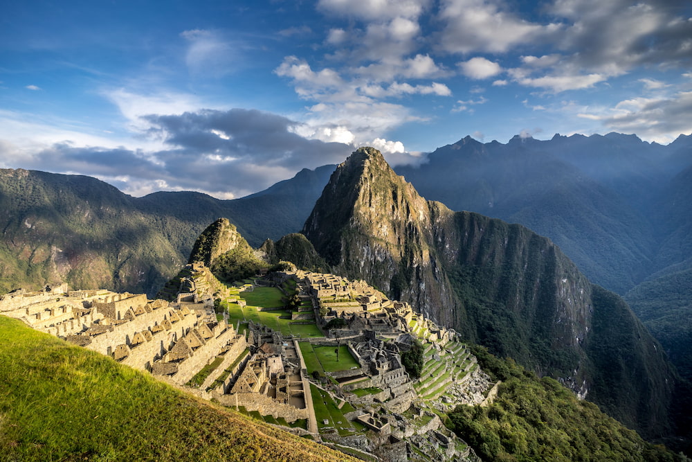The ruins of Machu Picchu surrounded by green mountains and early morning clouds.